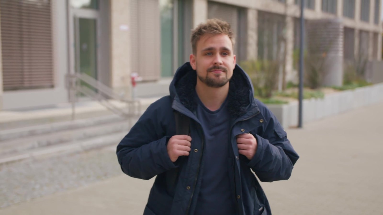 Junger Mann mit Rucksack geht vor dem Berliner Jobcenter-Gebäude