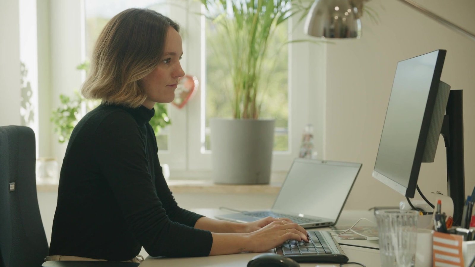 Sandra arbeitet konzentriert am Schreibtisch vor dem Bildschirm im hellen Büro
