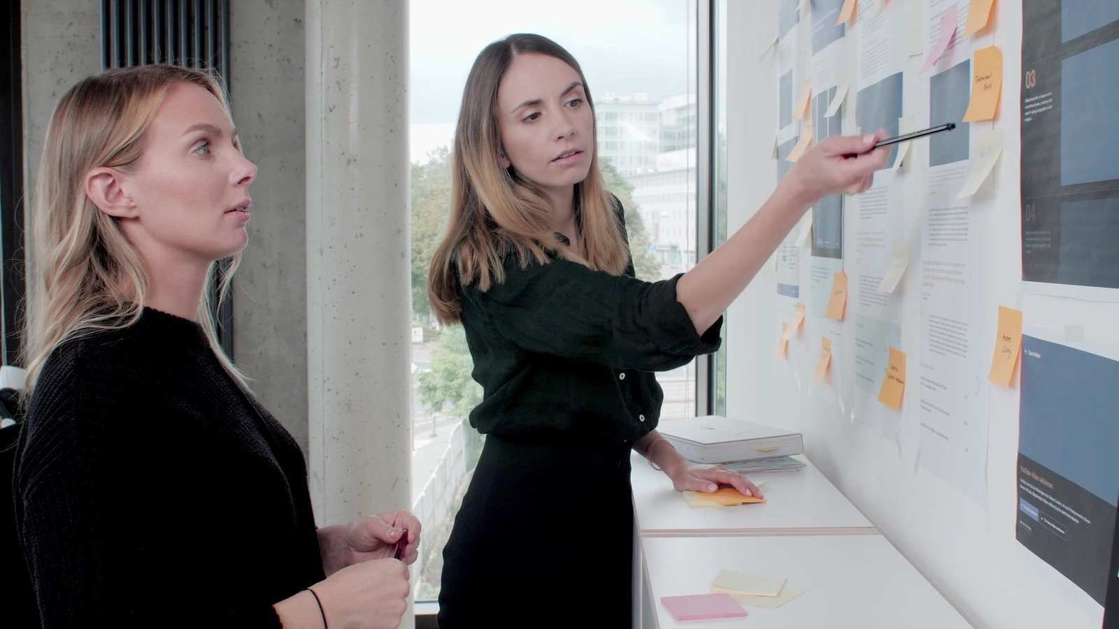 Zwei Kolleginnen besprechen Wireframes und Notizen an der Projektwand